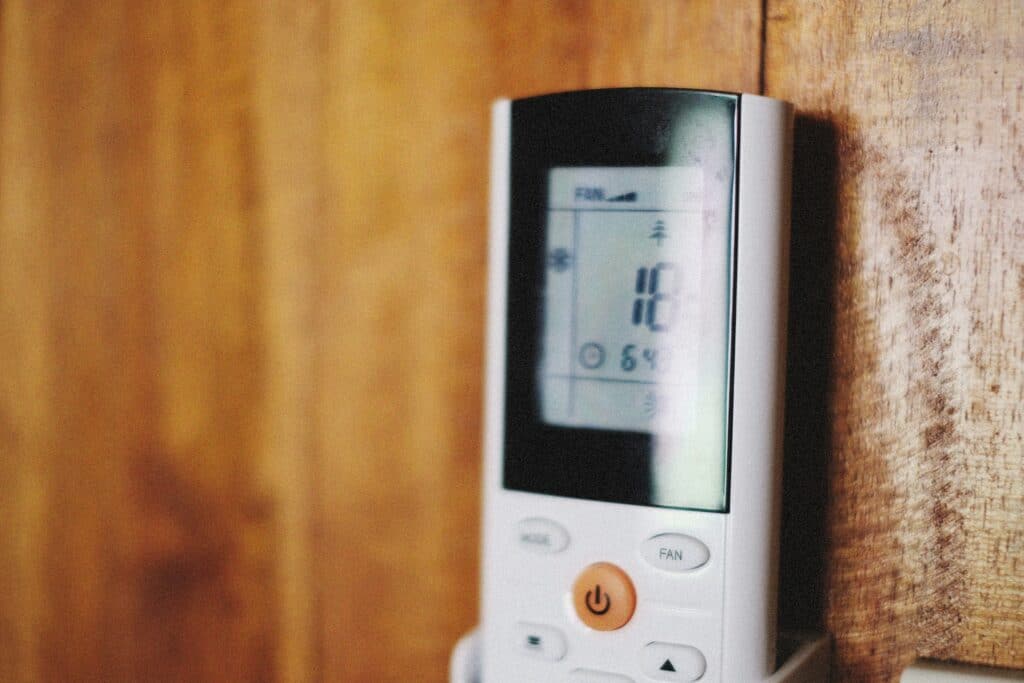 A close-up of a digital air conditioner remote control mounted on a wooden wall, displaying 18°C and fan settings—a perfect scene for the Bloomington Air Conditioning Summer Guide.